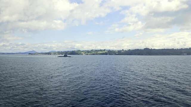 Distant view of a military submarine moving south from Haakonsvern near Bergen as a nearby vessel approaches in coastal waters