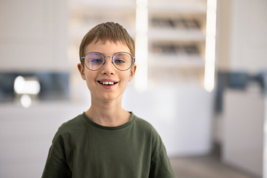 Smiling child boy standing in optician shop, posing for portrait wearing new eyeglasses, looking at camera. Eye care for childrens health, confidence through clear sight and stylish eyewear concept