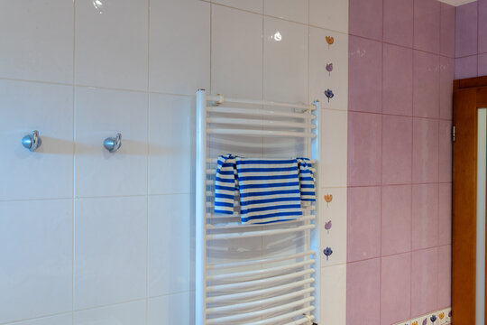Blue striped towel hanging on a white heated radiator against tiled bathroom walls