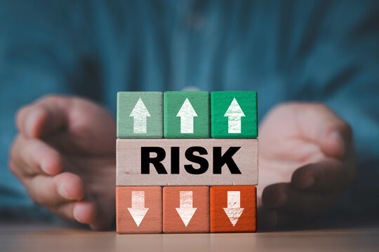 Risk management and business risk assessment concept with hands protecting wooden blocks, green upward and orange downward arrows for financial investment uncertainty decisions and risk control.