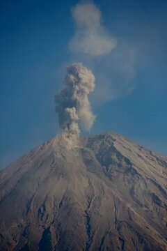 Mount Semeru volcano erupting with thick ash plume rising into deep blue sky, East Java, Indonesia
