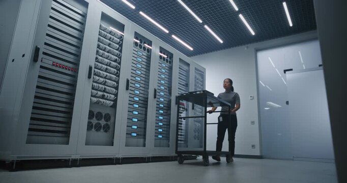 Female Data Center Technician Arrives With Utility Cart Carrying Network Switch, Opens Server Cabinet and Disconnects Cables For Hardware Replacement and Network Maintenance in Modern Facility.