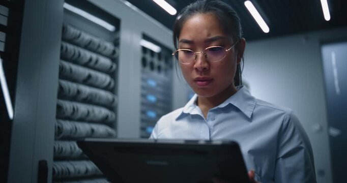Data Center Engineer Reviews Technical Data on Tablet Among Server Racks. Concerned Body Language Highlights System Analysis, Network Monitoring, Equipment Diagnostics and Operational Risk Management.
