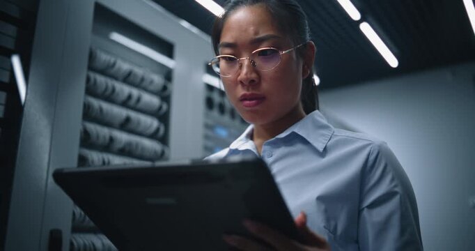 Female Technology Specialist Observes Tablet Screen in Server Room With Serious Expression. Scene Illustrates Data Center Monitoring, Problem Detection, Network Analysis and IT Decision Making.