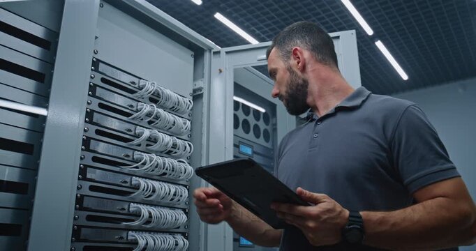Male Server Room Specialist Reviews Server Metrics on Tablet While Inspecting Ethernet Ports and Connections, Supporting Reliable Network Performance, System Maintenance, and Digital Operations.