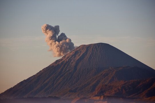 Mount Semeru volcano erupting with ash cloud at sunrise, warm light on volcanic slopes, East Java, Indonesia