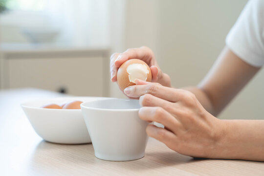 Close-up shot of woman hands peeling shell of boiled egg on the table.