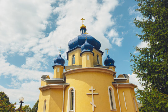 Yellow church with blue domes against a cloudy sky