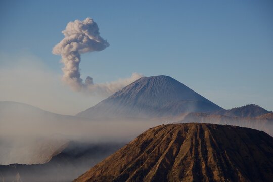 Mount Semeru volcano erupting with large ash plume above Mount Batok in morning haze, Bromo Tengger Semeru National Park, East Java, Indonesia