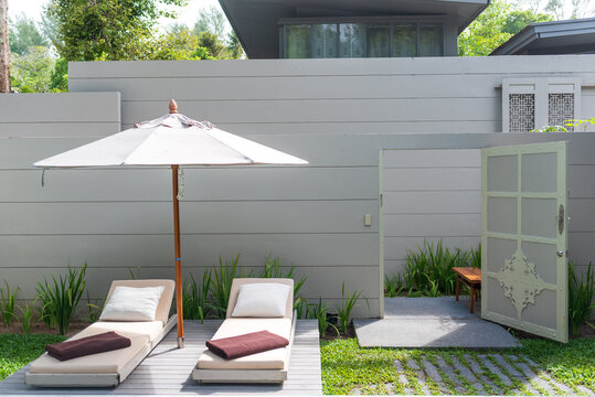 Sunbed loungers and patio umbrella on wooden deck near open garden door in tropical hospitality resort