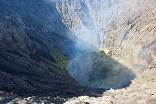 View from the rim into the active crater of Mount Bromo volcano with sulfur deposits, volcanic gas and steep eroded walls, East Java, Indonesia