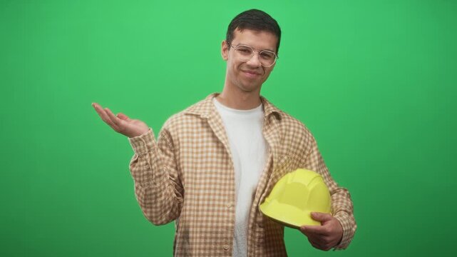 Man holding yellow hardhat with palm up gesture, construction worker in studio; confidence safety awareness.