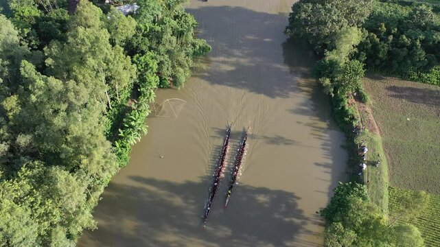 Sirajganj, Bangladesh - 07 September 2021: Aerial view of traditional long boats racing on the river surrounded by lush green trees and agricultural fields.
