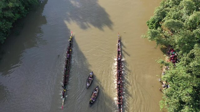 Sirajganj, Bangladesh - 07 September 2021: Aerial view of a traditional boat race on the river with many rowers in long wooden boats and spectators on the bank.