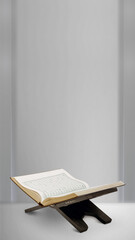 Holy Quran open on a traditional wooden stand (rehal) against a clean minimalist gray wall with copy space for Islamic holiday greetings background. © Leo Lintang