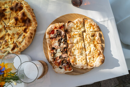 Top view of sliced pinsa pizza on wooden platter at garden table