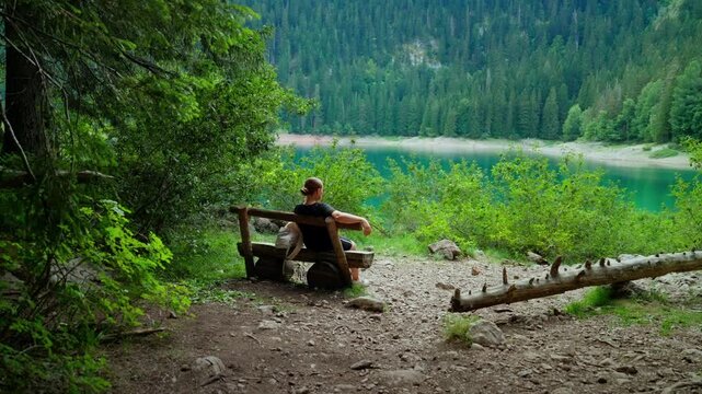 Tranquil forest lakeside bench with solitary hiker relaxing and contemplating nature, surrounded by lush green trees, calm water, and peaceful wilderness scenery