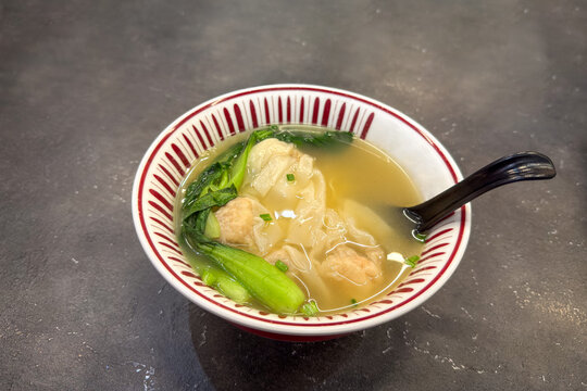 Wonton or pork dumplings soup in a bowl with bok choy, ready to eat. 