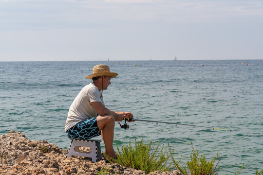 Man sitting alone on shore with a fishing rod, immersed in calm atmosphere of sea. Solitude, tranquility and slower pace of life