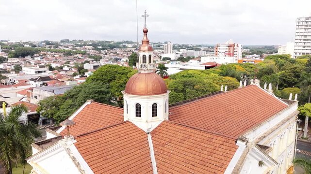 Araras, Brazil - 17 October 2026: Aerial view of the church dome with its distinctive copper roof surrounded by lush green trees and urban buildings in the city center.