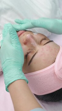 close-up of young woman receiving facial treatment with gloved hands applying cream to forehead, cheeks,