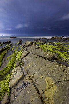Night landscape of Barrika beach flysch rock formations under a dark blue starry sky and ocean waves in Biscay Basque Country Spain