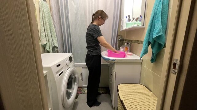 Woman cleans hands in basin. Woman thoroughly washes her hands using pink basin in warm bathroom. Lady carefully cleans her hands in vibrant pink basin within cozy bathing environment