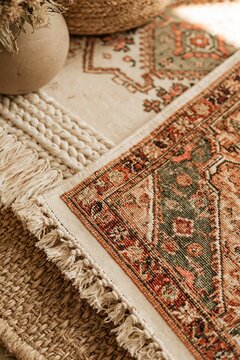 Closeup of faded patterned rug layered over woven jute and braided textile surfaces