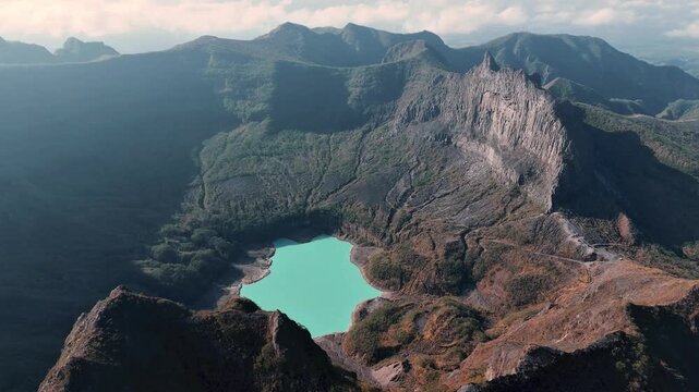 Kecamatan Ngancar, Indonesia - 16 September 2024: Aerial view of Kawah Gunung Kelud crater lake with turquoise water surrounded by rugged volcanic peaks and rocky slopes.