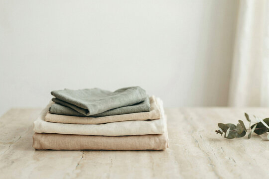 Folded linen cloths in sage and cream stacked on stone