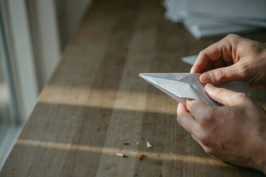 Two hands creasing a paper plane on a scuffed workbench