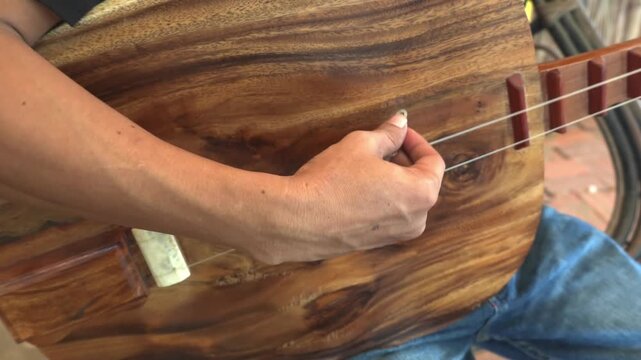 Static 4K close-up with live audio of musician hand strumming strings of traditional Cambodian Chapei Dang Veng lute in Siem Reap, Cambodia