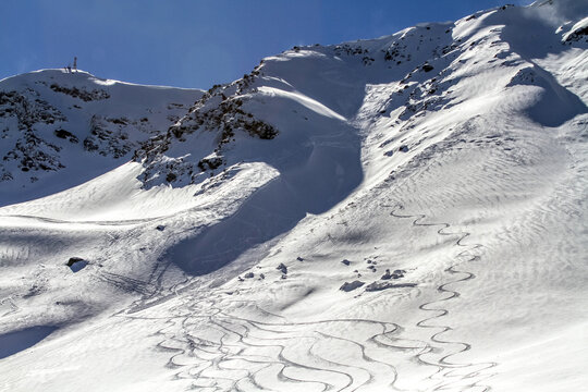 Winding ski tracks crisscross a sunny mountain slope
