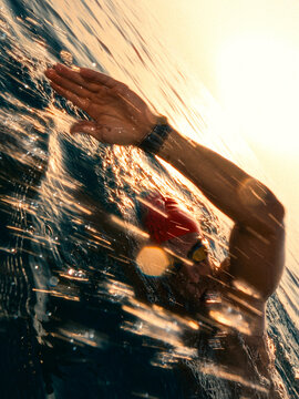Swimmer wearing a red cap strokes through open water at sunset