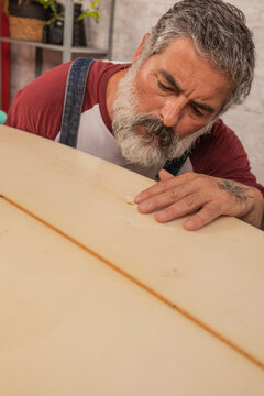 Surfer man inspecting surfboard damage preparing for repair
