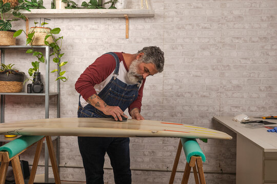 Surfer man shaping surfboard in home workshop
