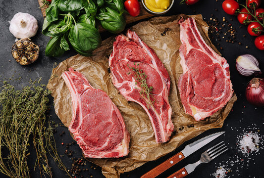 Three raw beef steaks on a wooden chopping board, garlic and a sprig