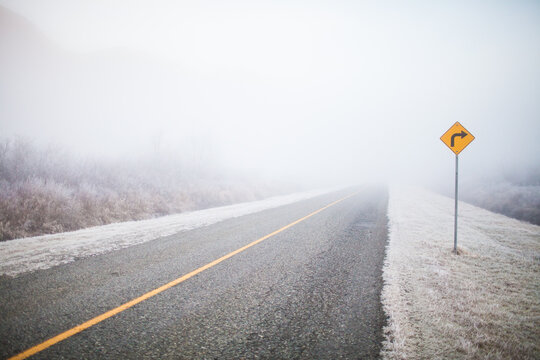 Country road with a turn sign in heavy morning fog