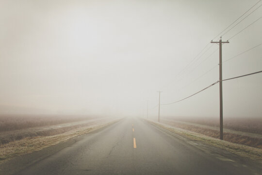 Foggy landscape with rural road with electrical wires on pole.