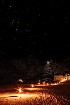 Torches showing the way to Berghaus Maennlichen in Grindelwald, Switzerland at night in winter with Moench, Tschuggen and Jungfrau mountain in the background against sky full of stars