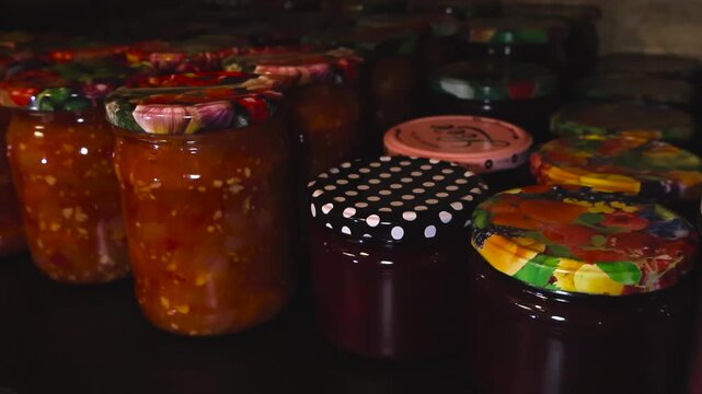 Rows of sealed glass jars with homemade preserved vegetables, possibly a spicy tomato and garlic relish, stored on a dark shelf in a pantry or cellar for winter food supplies