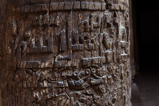Carved wooden column with Arabic calligraphy inside the Juma Mosque in Khiva, Uzbekistan. Ancient weathered pillar detail ideal for heritage, travel, and cultural publications.