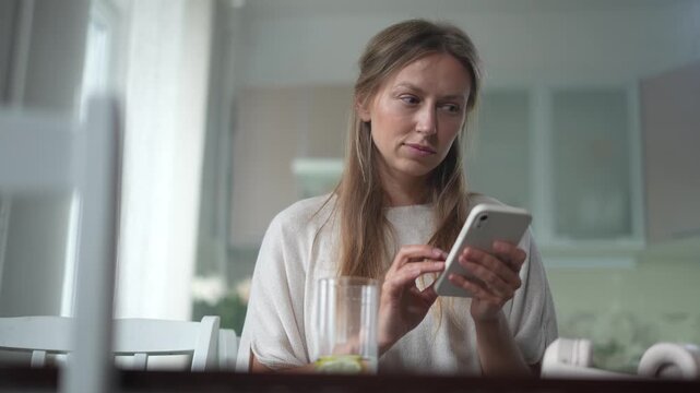 Young woman sitting at a table typing on her smartphone and nodding in agreement