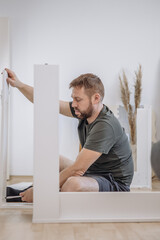Young man installing vertical part of white bookshelf assembling flat pack furniture at home © Katharina