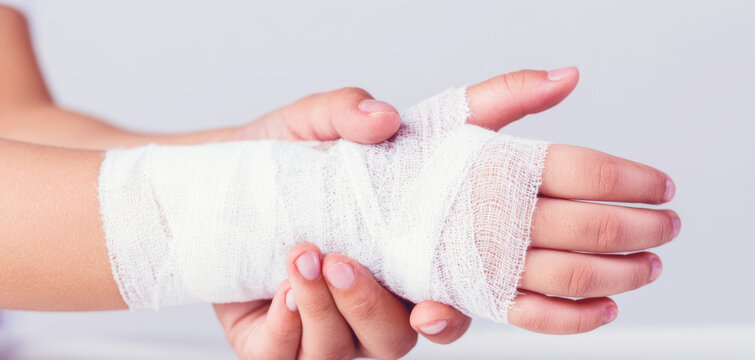 Young child supporting a gauze wrapped hand, receiving basic first aid and care while recovering from an injury