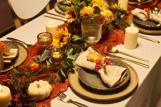 High angle shot of autumn festive dining table setting featuring pumpkins, candles, floral arrangements and tableware. Image suitable for Thanksgiving holiday promotion and catering marketing