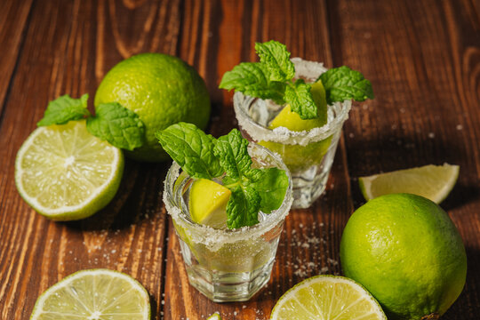 Tequila cocktails with mint and lime wedges on a wooden table