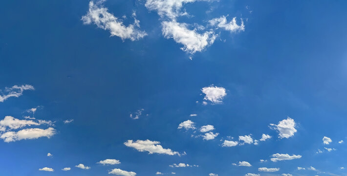 Panorama of isolated small clouds hanging over ordinary city buildings. Randomly scattered cloud on blue background. Clear fine summer day in capital.