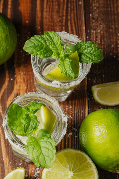 Two tequila cocktails garnished with mint and lime wedges on a wooden background