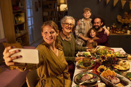 Multi-generation Caucasian family taking selfie with smartphone during festive dinner celebration. Useful for holiday marketing, family connection campaigns, telecom advertising
